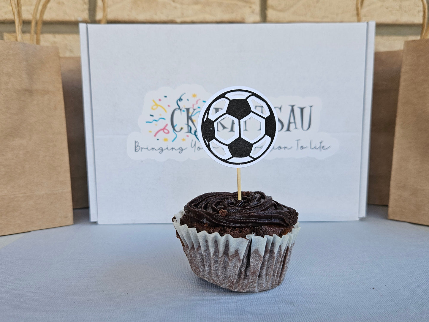 Chocolate cupcake with a soccer ball topper in front of a branded box.