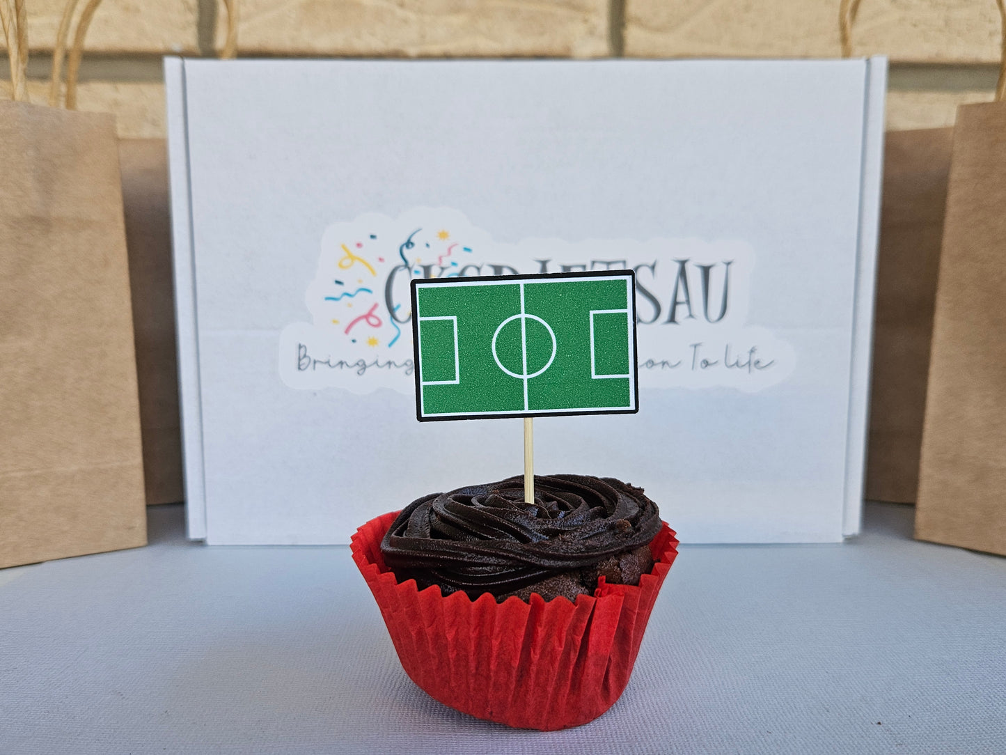 Chocolate cupcake with a soccer field topper in front of a branded box