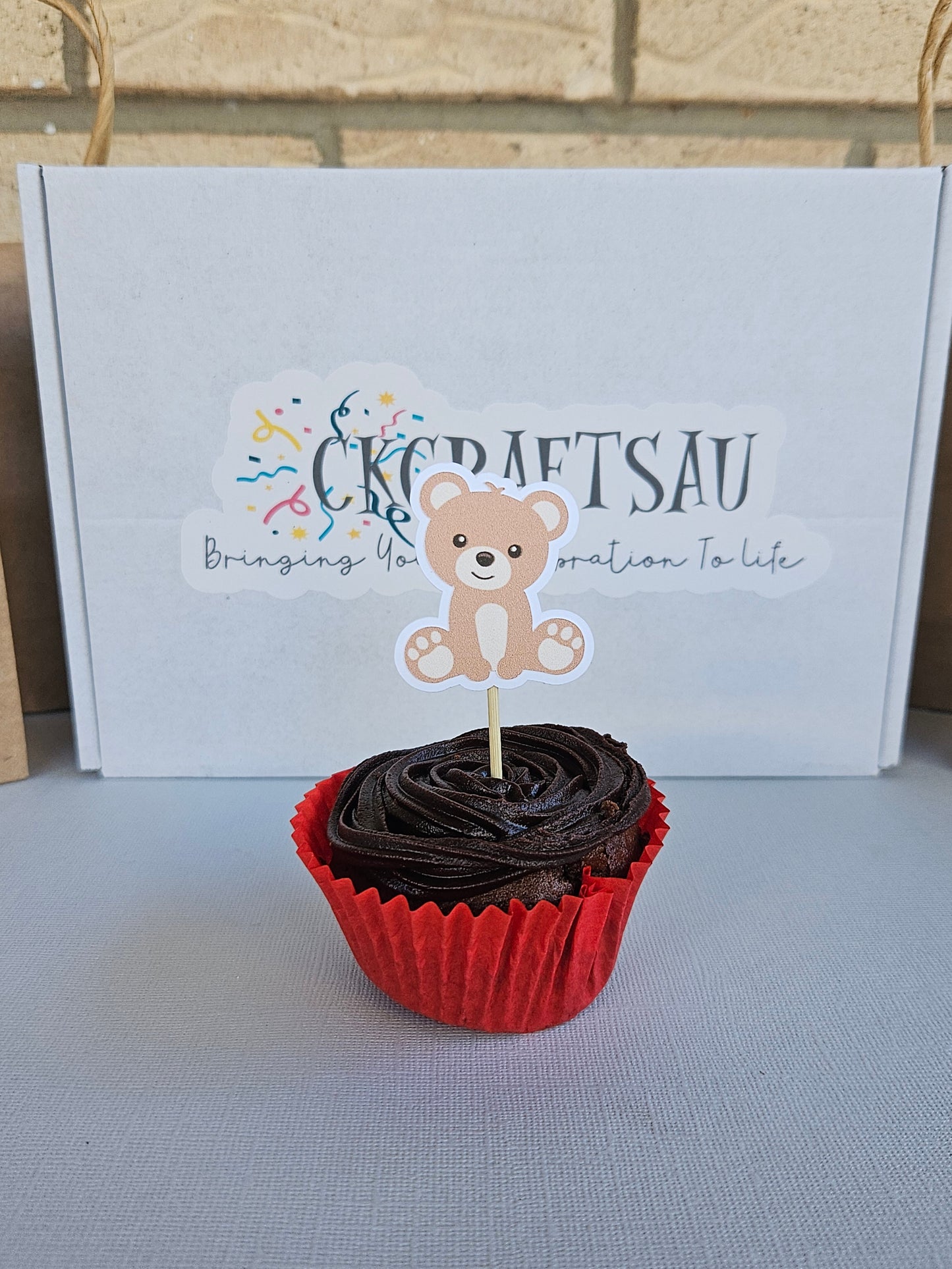 Cupcake with red paper liner with teddy bear design on a white branded box