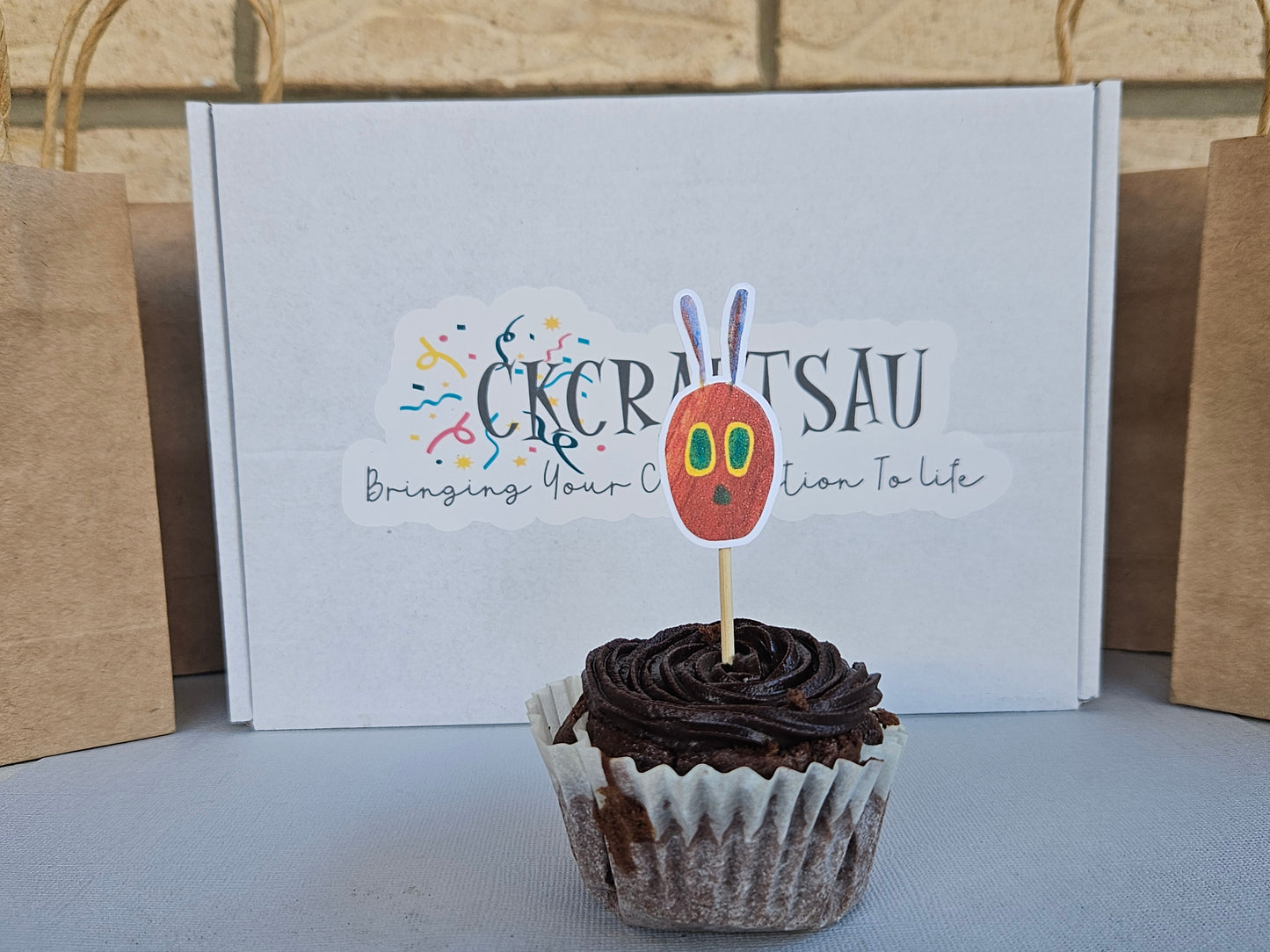 Cupcake with a decorative topper in front of a box with branding.