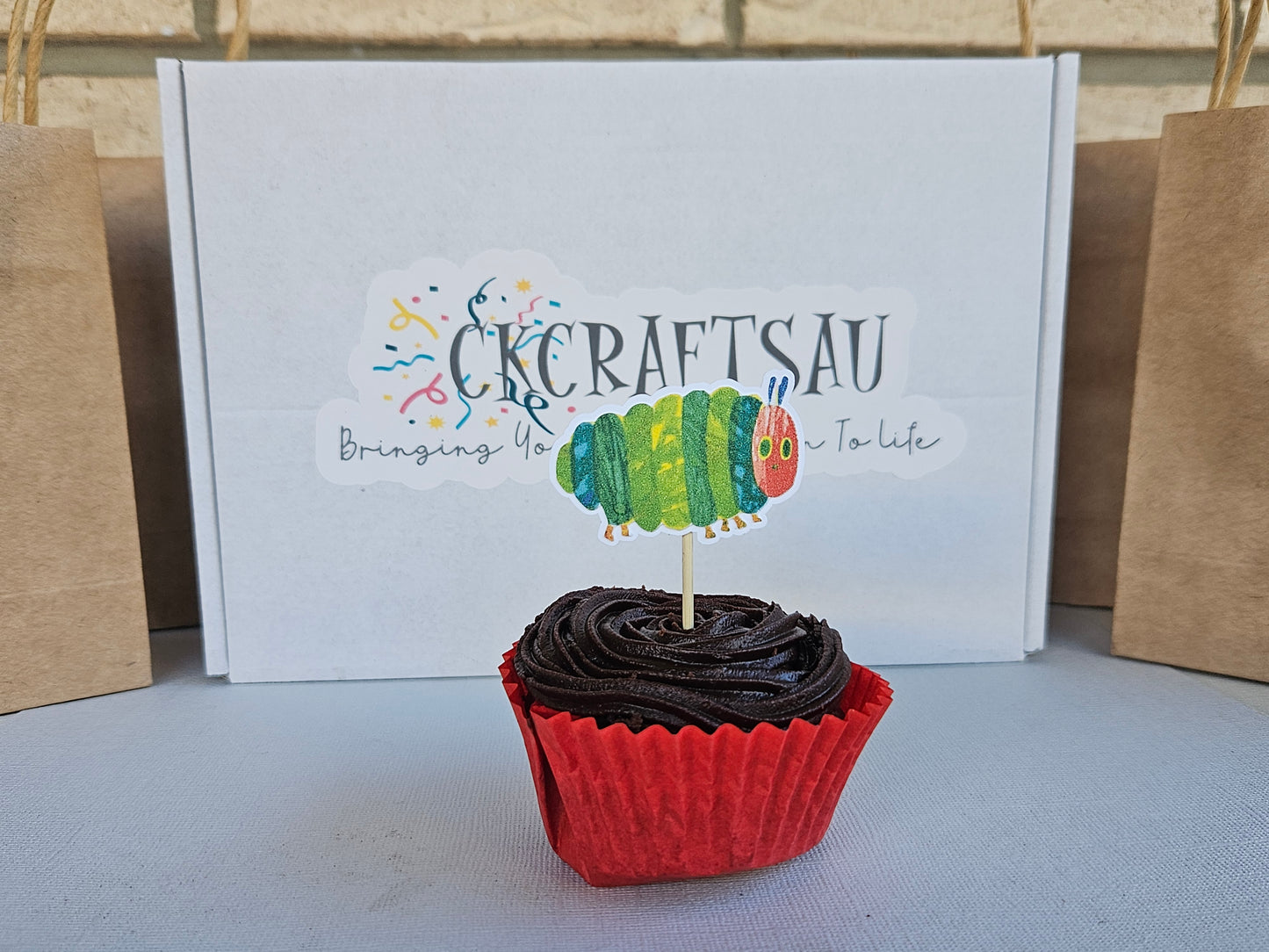 Cupcake with red wrapper and black frosting in front of a box with branding.