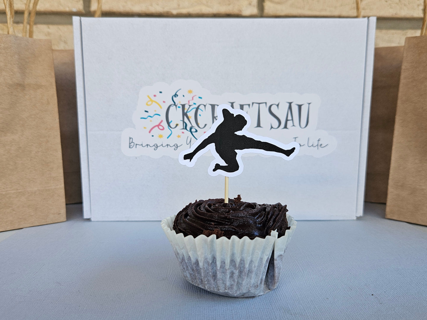 Chocolate cupcake with a silhouette topper in front of a box with branding.