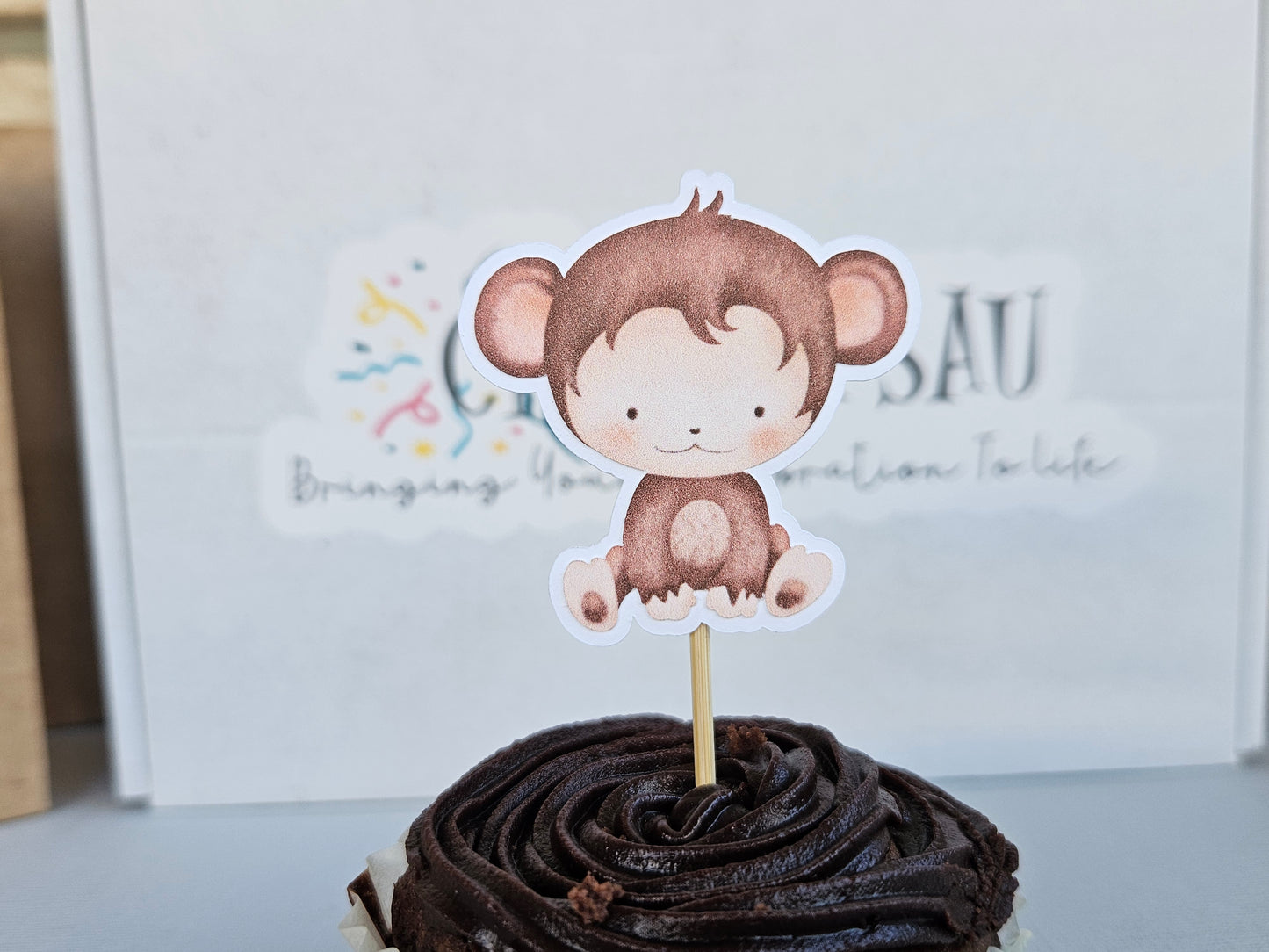 Chocolate cupcake with a monkey-themed topper on a white background