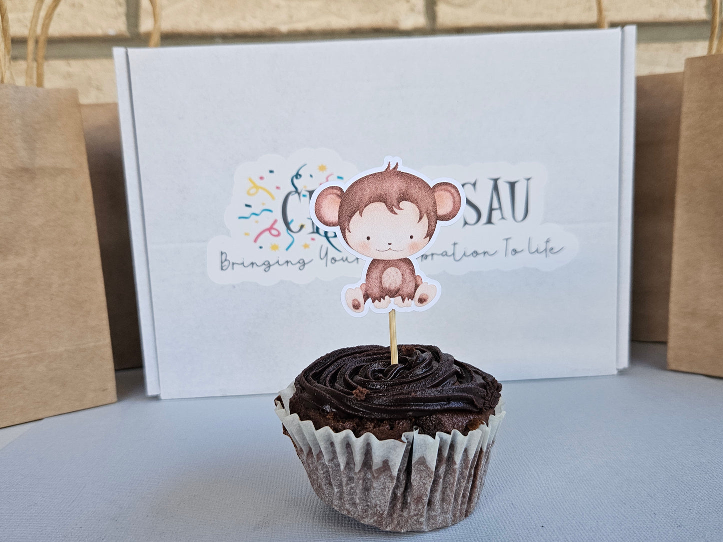 Chocolate cupcake with a monkey topper in front of a box with branding.