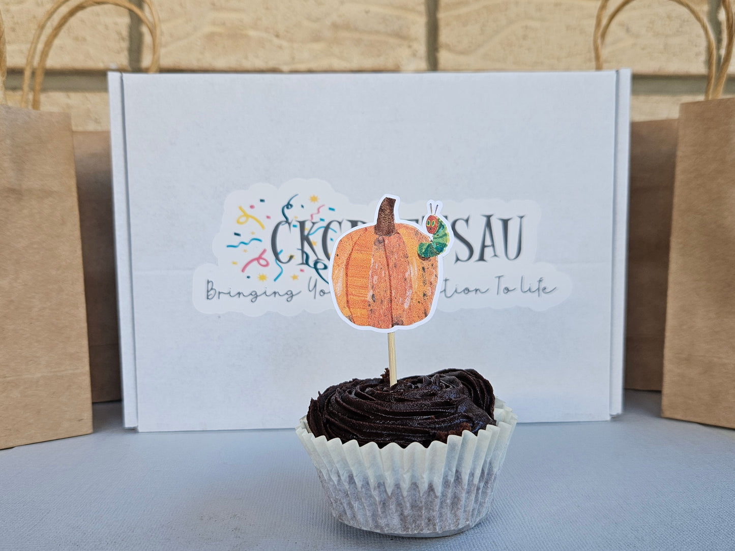 Cupcake with a pumpkin topper in front of a branded box