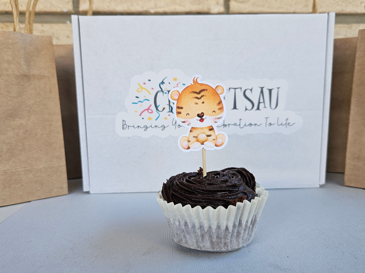 Chocolate cupcake with a tiger-themed topper in front of a white box with branding