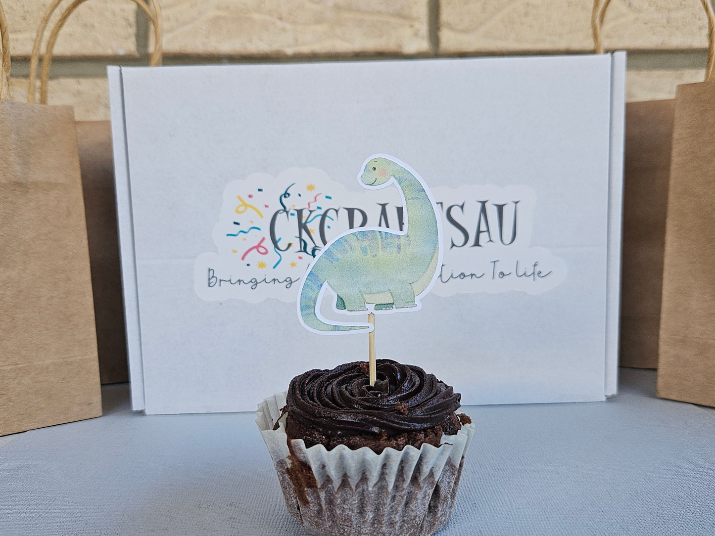 Cupcake with dinosaur-themed topper in front of a box with branding