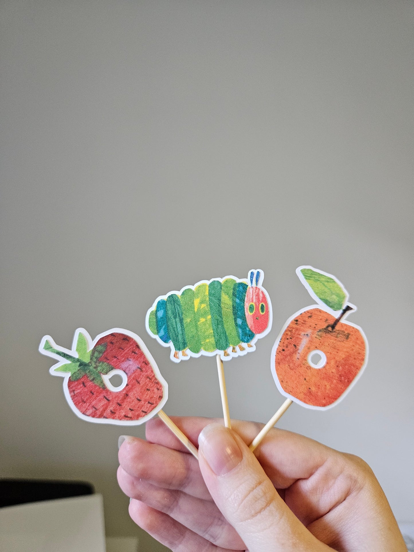 Hand holding a colorful caterpillar and fruit on a gray background
