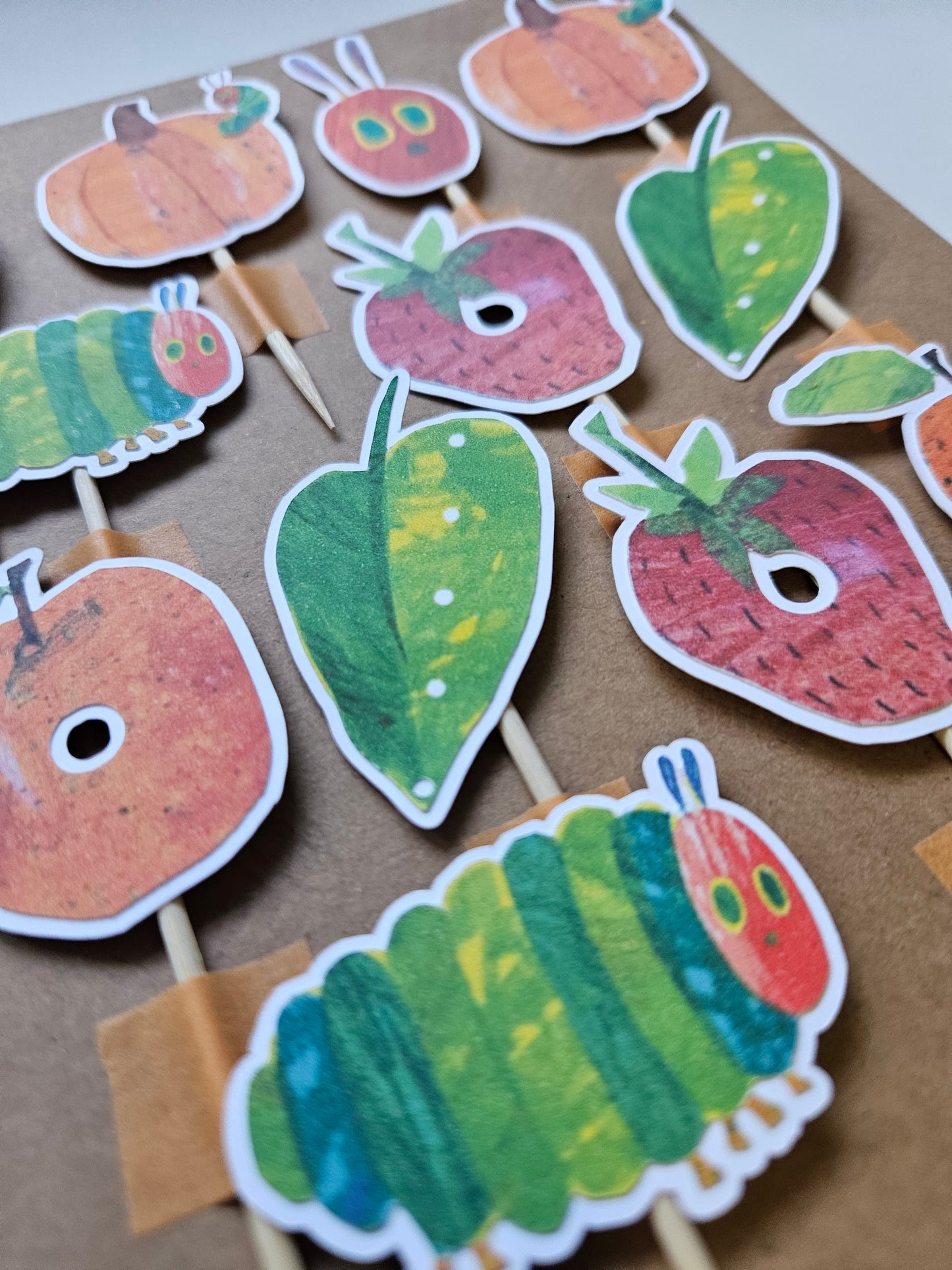 Set of colorful caterpillar and leaf cupcake toppers on a cardboard background