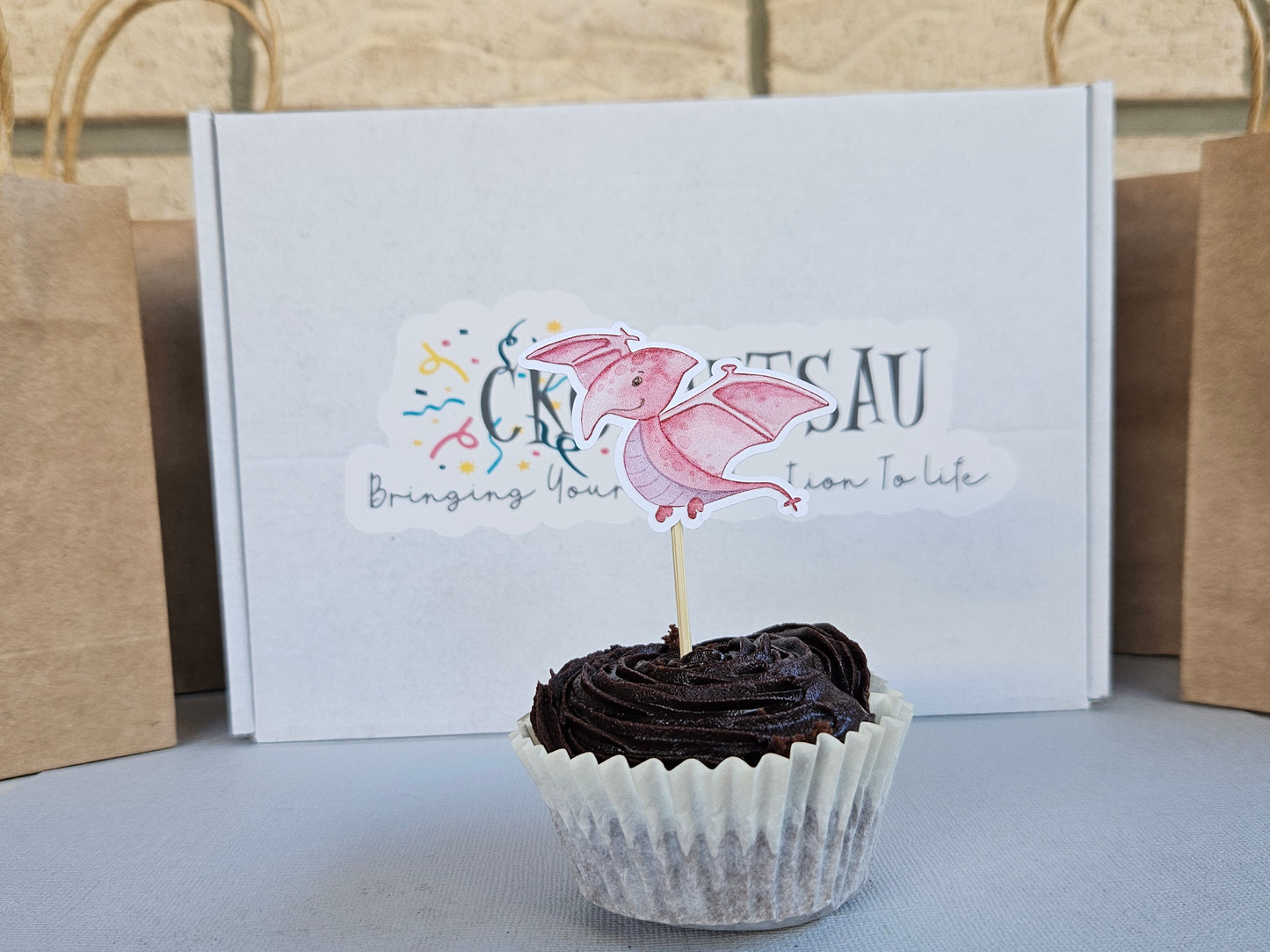 Chocolate cupcake with a dinosaur topper in front of a branded box