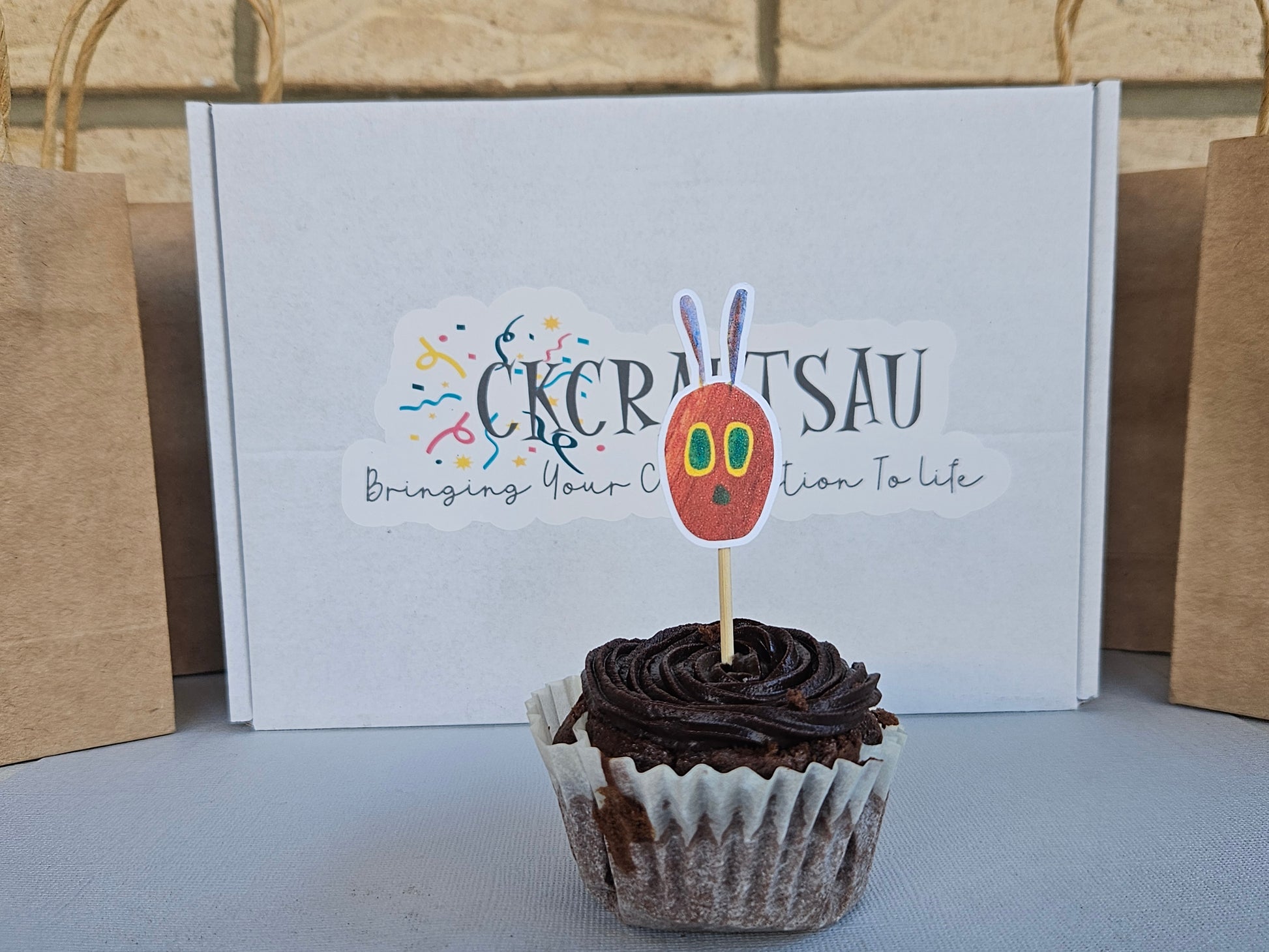 Cupcake with a decorative topper in front of a box with branding.