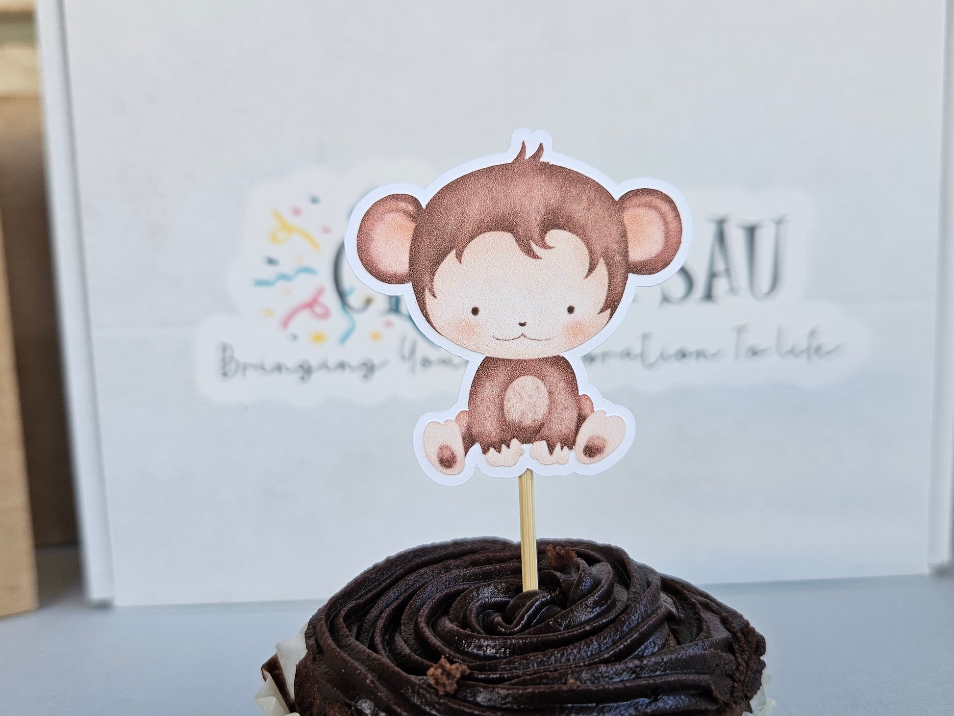 Chocolate cupcake with a monkey-themed topper on a white background